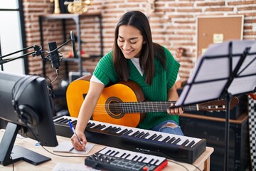 Young hispanic woman musician composing song playing classical guitar at music studio
