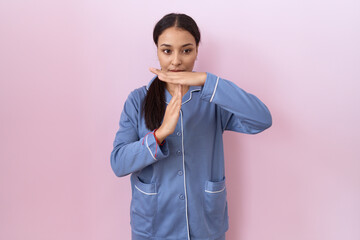 Young arab woman wearing blue pajama doing time out gesture with hands, frustrated and serious face