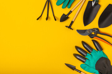 Gardening tools on a yellow background in a greenhouse. Spring in the garden. Garden shovels and rakes, secateurs, gloves for gardening on a bright background. Flat lay. Gardening and hobby concept.