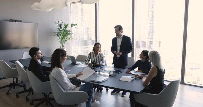 Millennial businessman in suit makes speech standing in front of company clients, investors or partners, take part in formal meeting, corporate training for staff members, commercial deal discussion
