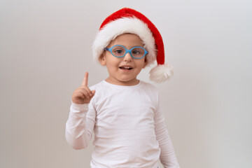 Fototapeta na wymiar Little hispanic boy wearing glasses and christmas hat smiling happy pointing with hand and finger to the side