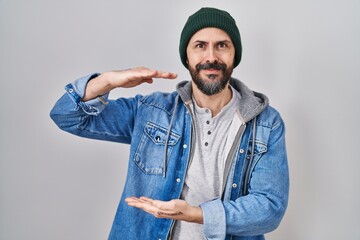 Obraz premium Young hispanic man with tattoos wearing wool cap gesturing with hands showing big and large size sign, measure symbol. smiling looking at the camera. measuring concept.
