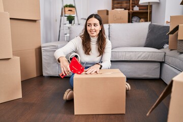 Young beautiful hispanic woman smiling confident packing cardboard box at new home