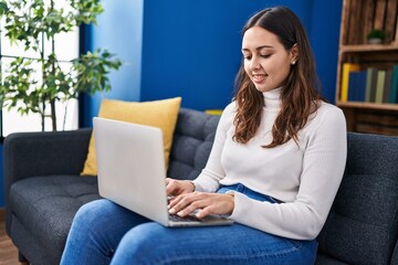 Young beautiful hispanic woman using laptop sitting on table at home