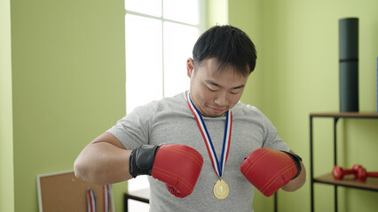 Young chinese man doing strong gesture wearing medal at sport center