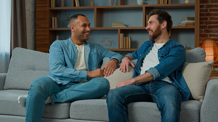 Two diverse 30s men businessmen talking at home on sofa multiracial friends companions african...