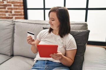 Down syndrome woman using touchpad and credit card sitting on sofa at home