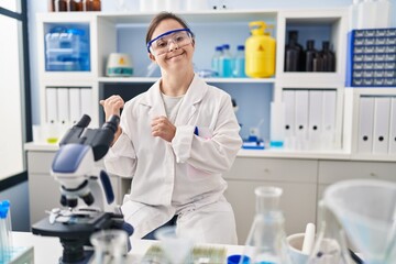 Hispanic girl with down syndrome working at scientist laboratory pointing to the back behind with...