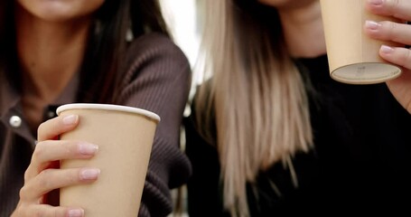Young women enjoying coffee on street. Low angle handheld shot of young girlfriend smiling and sipping coffee to go while spending summer weekend day on city street
