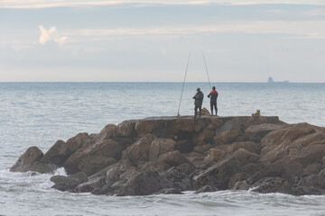 Anglers stand on a rock in the middle of the sea during the day