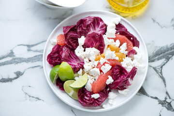 Plate with radicchio, goat cheese and citrus salad, horizontal shot on a white marble background