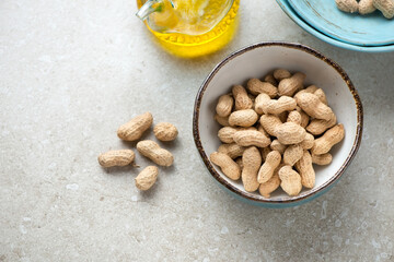 Peanuts in a bowl on a beige stone background, horizontal shot with space, high angle view
