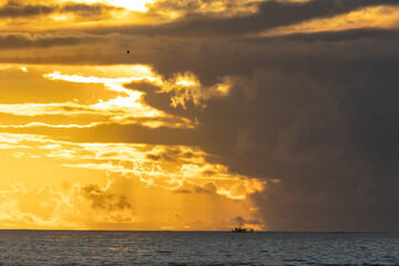 Landscape of bright yellow sunset sky over the dark sea - a boat sails in the distance