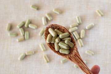 Vitamin from broccoli sulforaphane in capsules in a wooden spoon on a beige background. Tablets and...