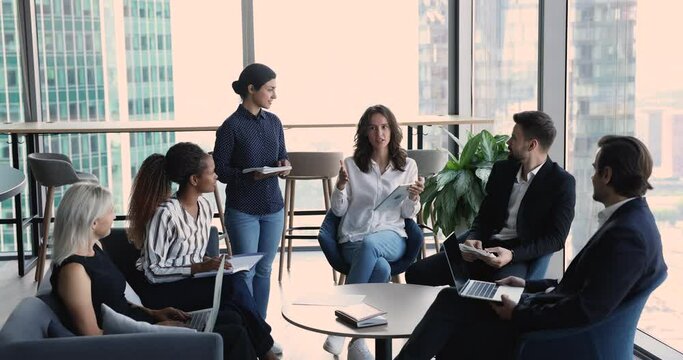 Diverse staff discuss collaborative project take part in group meeting, team leader share opinion at morning briefing with colleagues, gather together in modern office space. Brainstorming, teamwork