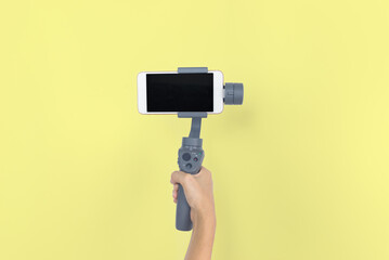Hand holding gimbal or stabilizer with mobile phone on yellow pastel background. Vlog and travel concept. copy space. Video mobile.