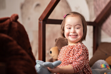 happy girl with down syndrome at home in the bedroom on the bed smiles, plays toys