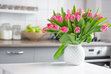 a bouquet of tulips in a white vase stand on the kitchen table. Kitchen background - obrazy, fototapety, plakaty