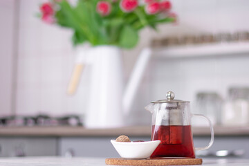 a glass teapot with tea and dessert stands on a white kitchen table against the background of a kitchen interior Close up