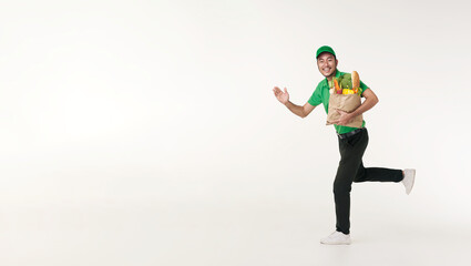 Asian delivery man wearing in green uniform holding fresh food paper bag and running isolated over white background. express delivery concept.