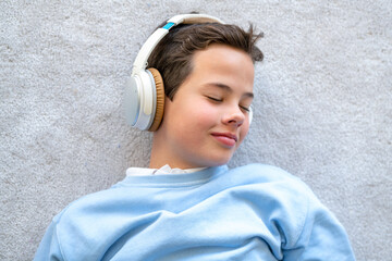 Child wearing headphones listens to music. Cute boy listening to music in earphones lying on floor.