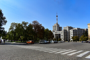 Fototapeta na wymiar Wide and long street with parked cars. Pedestrian crossing going towards the park with fountainsUkraine, Kharkiv. Freedom Square. Derzhprom building (House of State Industry). 