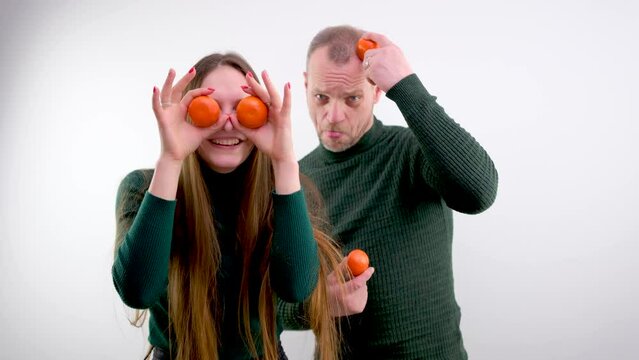 young girl put Tangerines to eyes and pulled out tongue stuck out and she twists and makes faces in the background a man on a white background green sweater long hair joke fooling around grimacing
