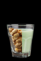 Pistachio milk and pistachios in glass on the black background. Creative collage. Close up