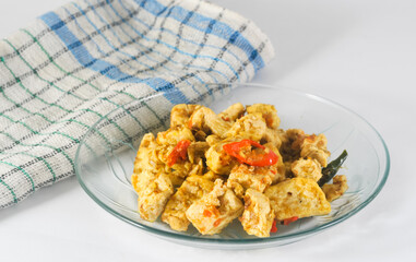 sliced tofu cooked dry with chilies served on a small plate with a napkin isolated on a white background