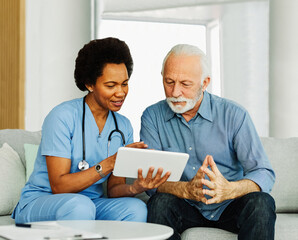 nurse doctor senior care tablet computer technology showing caregiver help assistence retirement home nursing elderly woman african american black happy laughing man