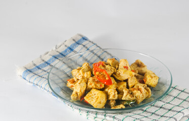 sliced tofu cooked dry with chilies served on a small plate with a napkin isolated on a white background