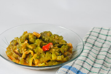 stir-fried bitter melon with sliced tempeh served in a small plate with a napkin isolated on a white background