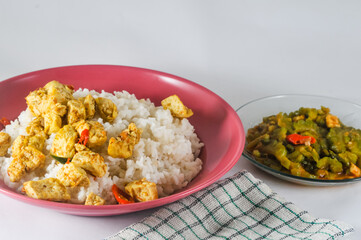 white rice with sliced tofu cooked dry with chilies and stir-fried bitter melon with sliced tempeh served in a small plate and a napkin isolated on a white background
