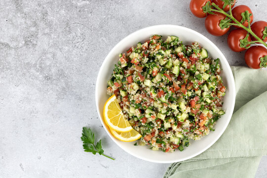Vegan salad with quinoa, cucumbers, tomatoes, parsley on a gray background. Tabouleh salad. Top view. Copy space. 