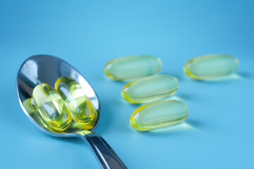 Bright yellow golden fish oil capsules and silver teaspoon on blue background. Vitamin D and...