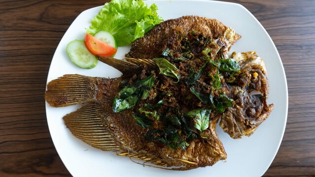 Dry fried gourami or gouramy or gurami goreng seasoned with green chilies on a white plate. In general, this menu can be found in Indonesian seafood restaurants