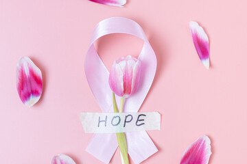 Pink ribbon with tulip and petals on a pink background.