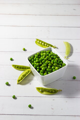 Fresh organic peas in a white bowl on a white wooden background. Healthy food concept.