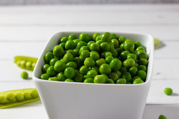 Close-up of organic peas in a white bowl on white wooden background. Concept of veganism, vegetarian and healthy food.