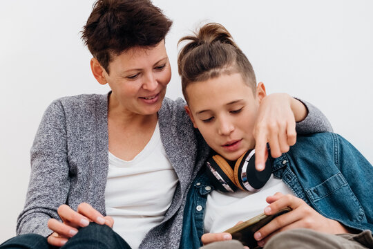 Middle aged mother spending time with teenager son together using mobile phone.