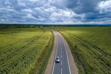 Aerial view of intercity road between green agricultural fields with fast driving car. Top view...