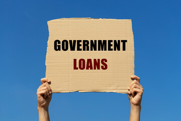 Government loans text on box paper held by 2 hands with isolated blue sky background. This message...