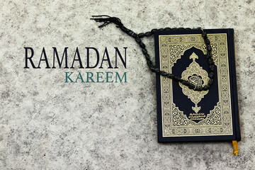 Holy Quran with Arabic calligraphy meaning of Al Quran and black rosary and Ramadan Kareem text 