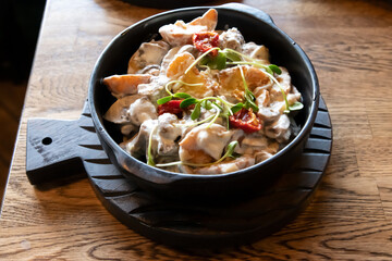 Close-up view of fried potatoes roasted with wild Porcini mushrooms on black plate on wooden table in restaurant. Soft focus. Food background theme.