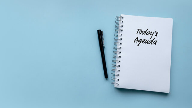 Top view of pen and notebook written with Today's Agenda on blue background with copy space.
