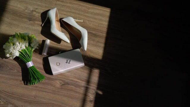 Wedding morning. A bride's bouquet of white flowers with a ribbon, women's high-heeled shoes, a purse or cosmetic bag, a diamond engagement ring, jewelry earrings and lipstick.