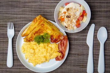 Kids menu, scrambled eggs, bacon, toast and muesli with yoghurt served on the restaurant table with plastic kids friendly eating utensil.