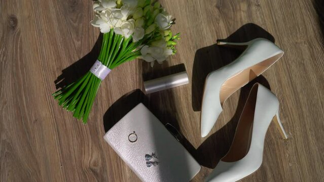 Wedding morning. A bride's bouquet of white flowers with a ribbon, women's high-heeled shoes, a purse or cosmetic bag, a diamond engagement ring, jewelry earrings and lipstick.