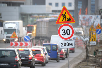 Roadworks warning traffic signs of construction work on city street and slowly moving cars