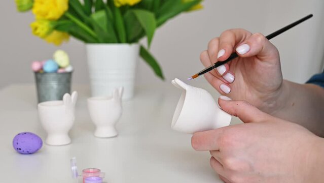 Woman paints bunny egg holder  for easter. Preparing for celebration.Pastel colors